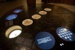 Stół ze stali w formie <br> powiększonej monety. <br>W otworach w blacie <br>umieszczone 4 lightboxy.<br> Gablota i monitory <br> zostały zamontowane <br> przez inne firmy